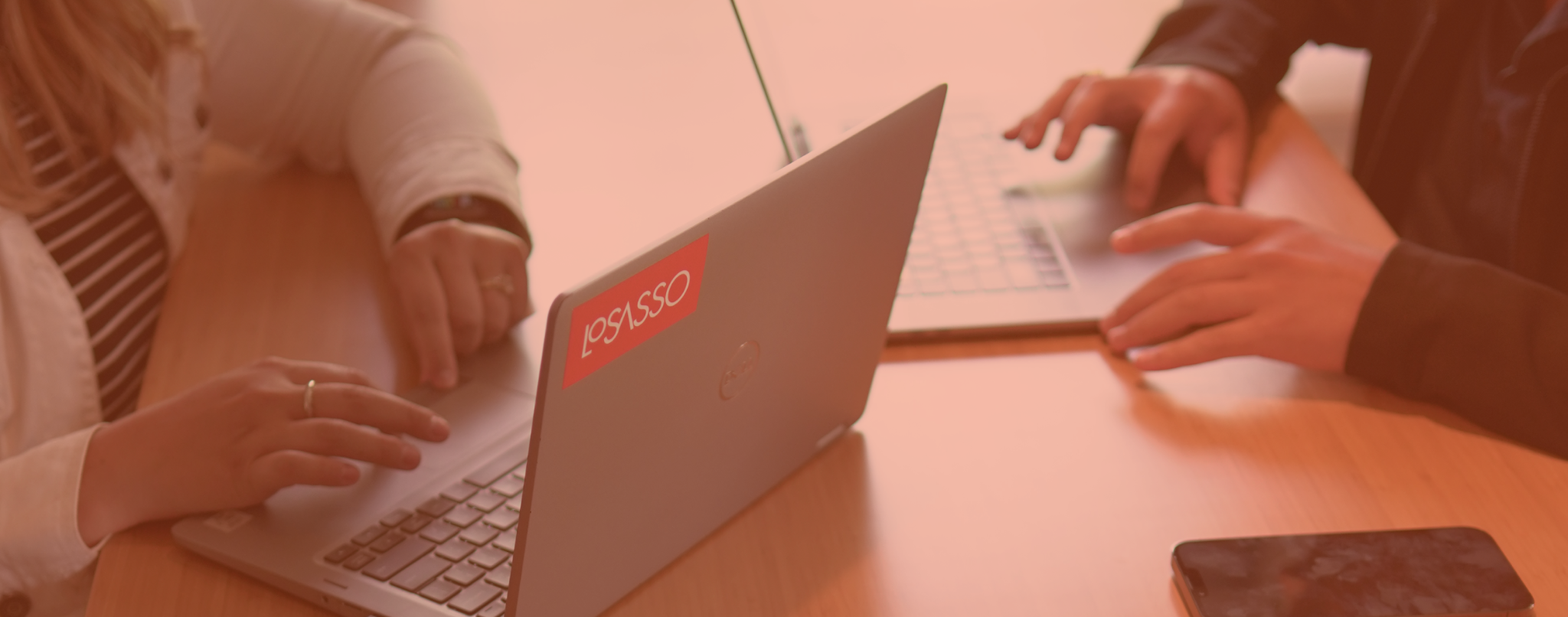 Hands working on laptops with a LoSasso Integrated Marketing sticker on the back